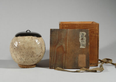 Ein Frischwassergefäß mizusashi aus Hagi-Keramik mit schwarzem Lackdeckel. Hier mit der dazugehörigen alten Holzdose.