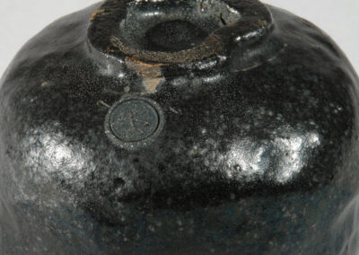 Eine schwarze Teeschale aus Raku-Keramik von Kichizaemon IX. Hier ein Blick auf den Fuß der Schale von schräg oben mit dem Raku-Siegel des Künstlers.