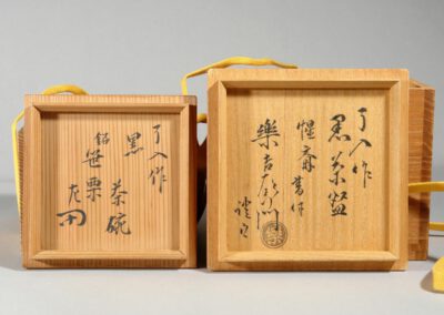Eine schwarze Teeschale aus Raku-Keramik von Kichizaemon IX. Hier die dazugehörigen Holzdosen und deren Beschriftung.